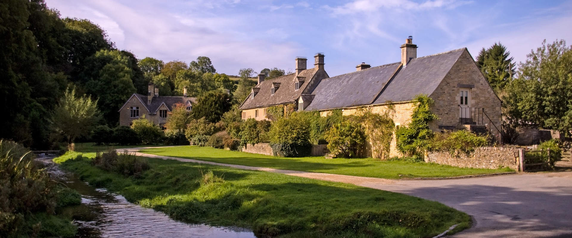 Honey-coloured Cotswold stone cottages beside a stream and country lane in Gloucestershire
